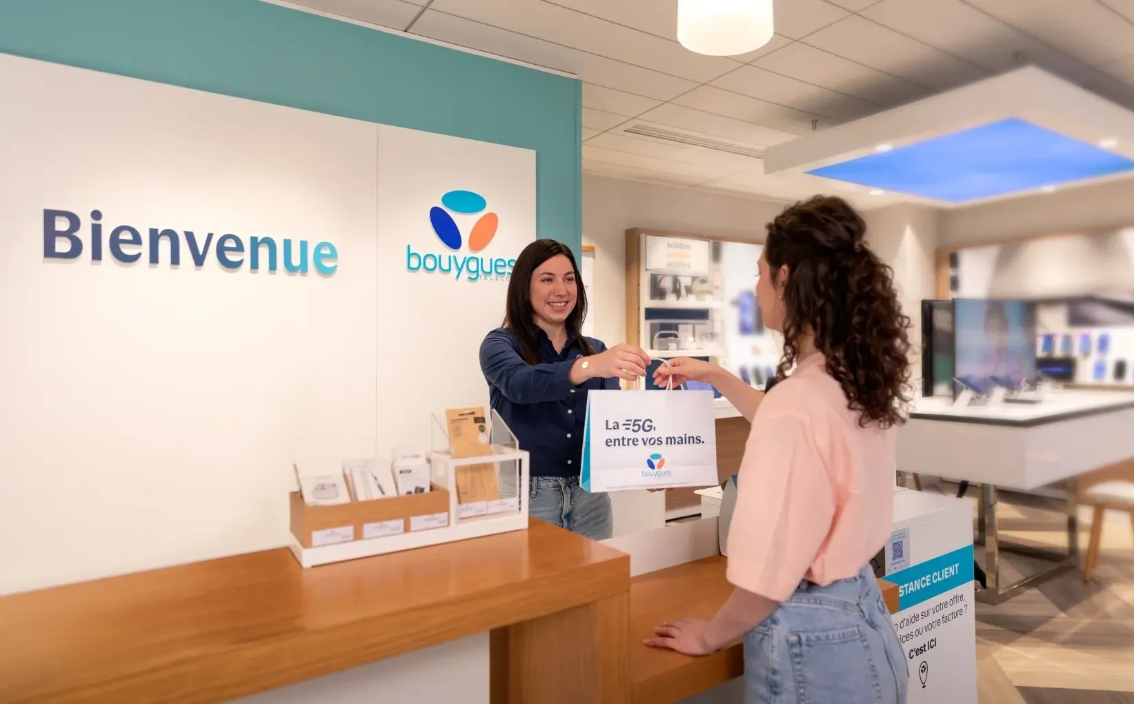 Vendeuse qui donne un sac bouygues telecom à une cliente en boutique