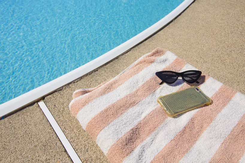 Smartphone posé sur une serviette de plage avec des lunettes, au bord d'une piscine
