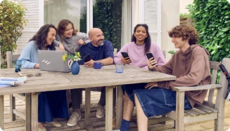 Cinq individus sur leurs ordinateurs portables et smartphones, réunis autour d'une table de jardin sur une terrasse.